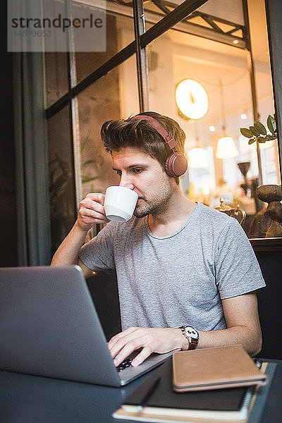 Selbstbewusster Geschäftsmann trinkt Kaffee  während er seinen Laptop am Schreibtisch im Büro benutzt