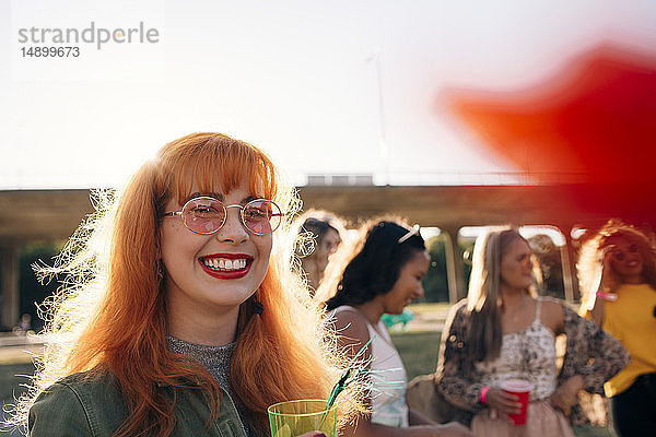 Lächelnde junge Frau trinkt während eines Konzerts mit Freunden