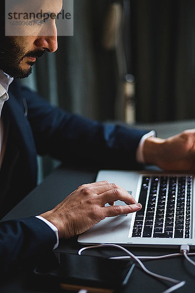 Selbstbewusster Geschäftsmann tippt am Laptop am Schreibtisch im Kreativbüro