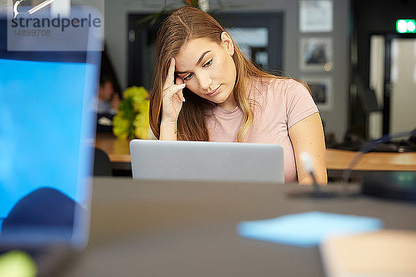 Angespannte kreative Geschäftsfrau schaut im Büro auf den Laptop