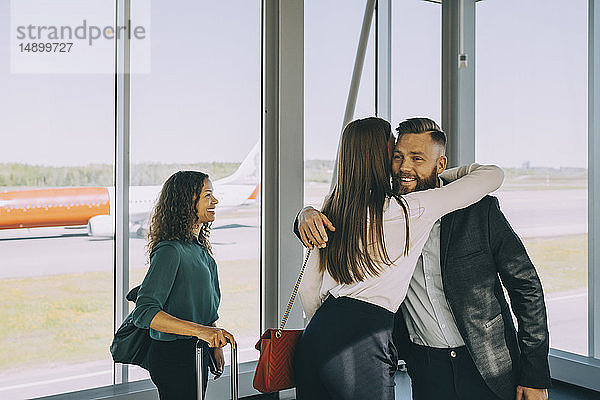 Lächelnde Geschäftsfrau schaut Kollegen bei der Begrüßung an  während sie im Flughafenkorridor steht