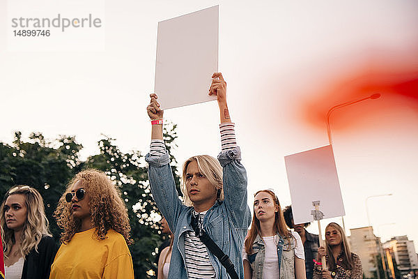 Junge Männer und Frauen protestieren mit Plakaten  während sie in der Stadt gegen den Himmel marschieren