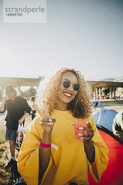 Porträt einer lächelnden Frau  die bei einem Drink gestikulierend am Musikfestival teilnimmt