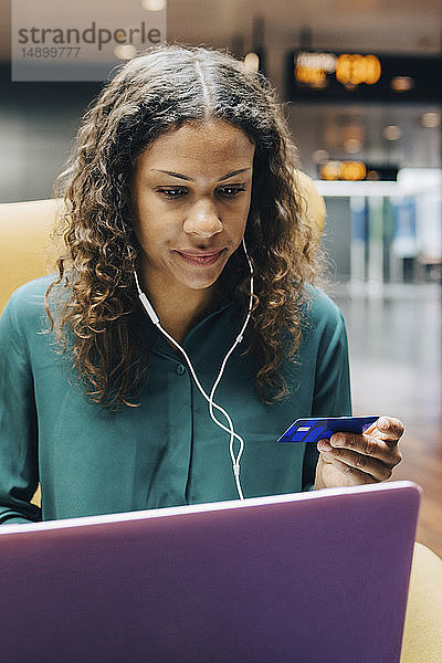 Zuversichtliche Geschäftsfrau mit Kreditkarte bei der Benutzung eines Laptops durch eine Kollegin in der Flughafen-Lobby
