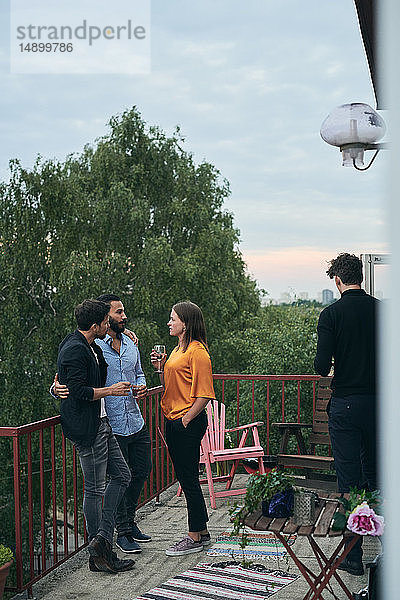 Freunde unterhalten sich in voller Länge  während sie während des geselligen Beisammenseins auf der Terrasse stehen
