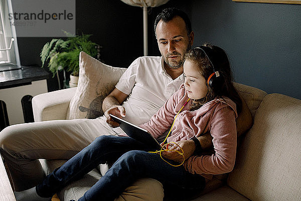 Vater hilft Tochter bei der Verwendung eines digitalen Tablets auf der Couch zu Hause