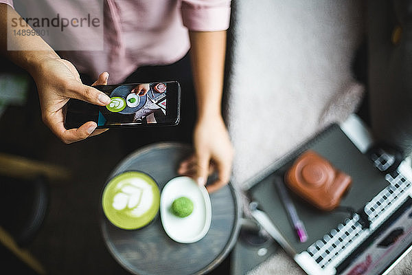 Mitschnitt einer weiblichen Bloggerin  die Matcha-Tee und Snack über ein Smartphone im Kreativbüro fotografiert