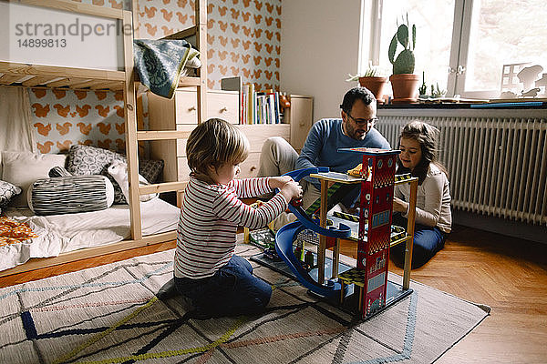 Mädchen spielt mit Spielzeugautos  während sich Vater und Schwester zu Hause im Schlafzimmer unterhalten