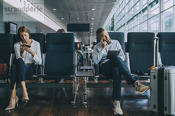 Nachdenklicher Geschäftsmann schaut weg  während er neben einer Kollegin im Wartebereich des Flughafens sitzt