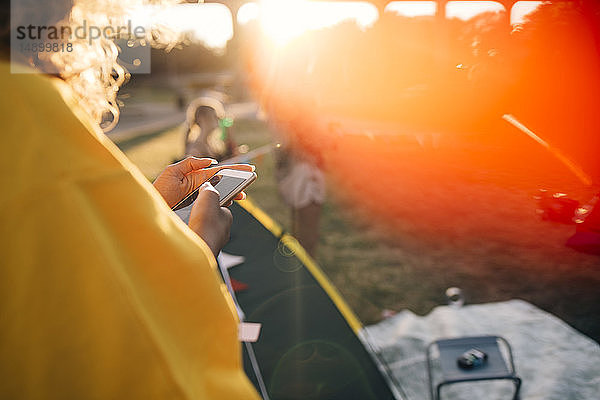 Ausgeschnittenes Bild einer Frau  die ein Mobiltelefon benutzt  während sie an einem sonnigen Tag am Zelt steht