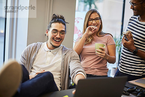 Fröhliche Unternehmer schauen auf den Laptop auf dem Schreibtisch im Kreativbüro