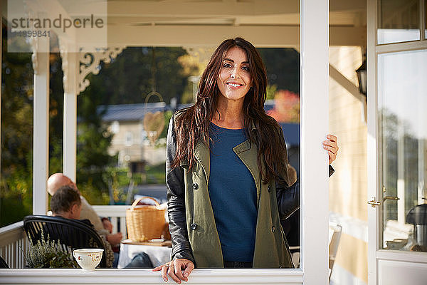 Porträt einer selbstbewusst lächelnden reifen Frau auf der Veranda stehend