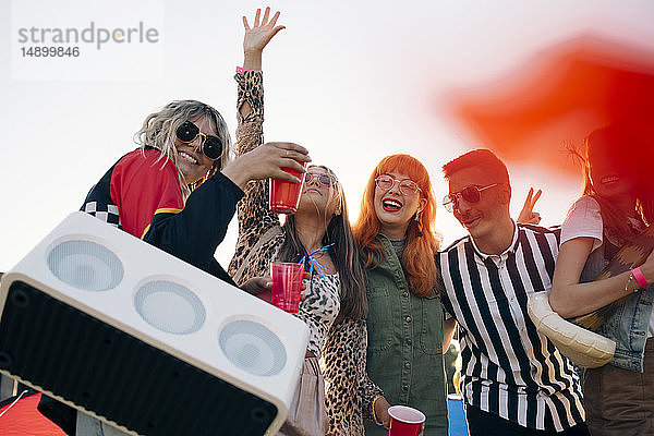 Glückliche Freunde mit Redner und Getränken beim Musikfestival gegen den Himmel