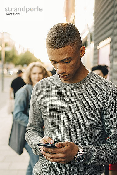 Teenager  der ein Mobiltelefon benutzt  während er in der Stadt auf der Straße steht