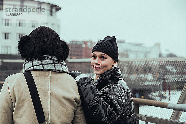 Porträt einer selbstbewusst lächelnden Frau in warmer Kleidung  die im Winter mit einem Freund in der Stadt steht