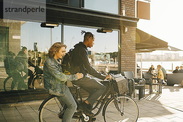Jugendlicher Junge fährt mit fröhlichem Freund bei Sonnenschein Fahrrad in der Stadt