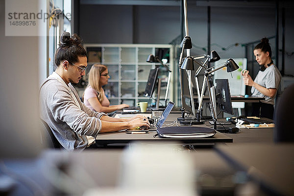 Männlicher Unternehmer mit Laptop am Schreibtisch im Kreativbüro