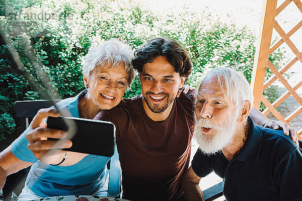 Lächelnder männlicher Hausmeister beim Selfie mit älterem Mann und Frau im Hinterhof