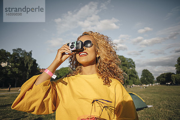 Lächelnde junge Frau fotografiert mit der Kamera auf dem Feld gegen den Himmel
