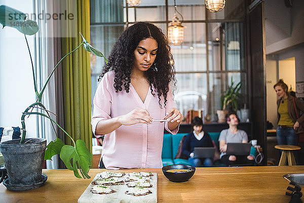 Selbstbewusste junge Einflussnehmerin fotografiert Kürbissuppe und Knäckebrot auf dem Tisch mit einem Smartphone im kreativen Off
