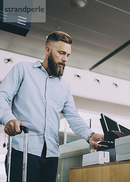 Niedrigwinkelansicht eines Geschäftsmannes beim Scannen eines Tickets auf einem Smartphone am Flughafen-Check-in-Schalter