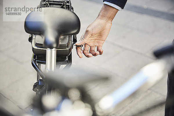 Abgehackte Hand eines männlichen Pendlers sperrt Elektrofahrrad in der Stadt