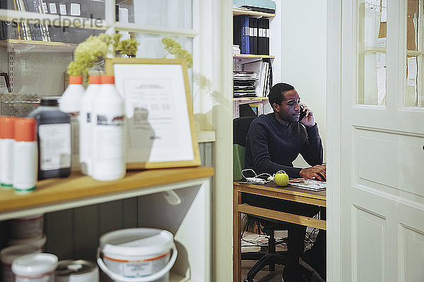 Selbstbewusster junger männlicher Ladenbesitzer am Schreibtisch sitzend am Smartphone