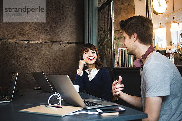 Lächelnde weibliche Fachkraft schaut den männlichen Kollegen an  während sie bei der Planung der Strategie während der Besprechung im Büro