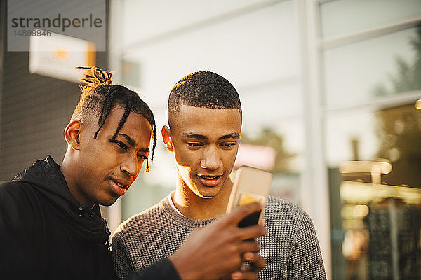 Teenager zeigt einem Freund in der Stadt bei Sonnenuntergang sein Handy