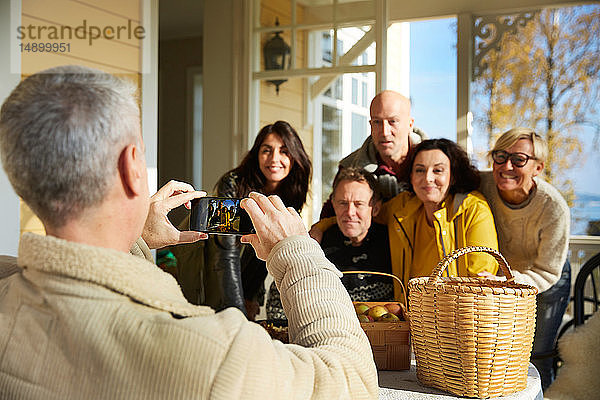 Reifer Mann fotografiert Freunde mit Smartphone auf der Veranda