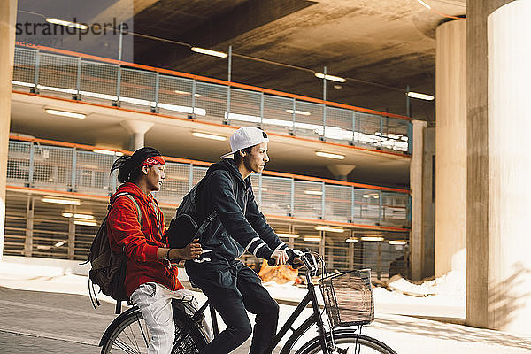 Seitenansicht eines jungen Mannes  der mit einem Freund in der Stadt Fahrrad fährt
