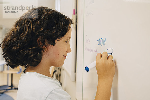Seitenansicht eines Jungen mit lockigem Haar beim Schreiben auf die Tafel im Klassenzimmer