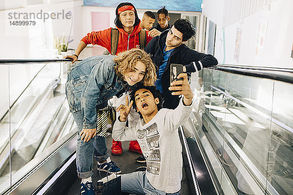 Glückliche männliche Freunde  die sich mit einem Smartphone auf dem Laufsteg eines Einkaufszentrums selbstständig machen
