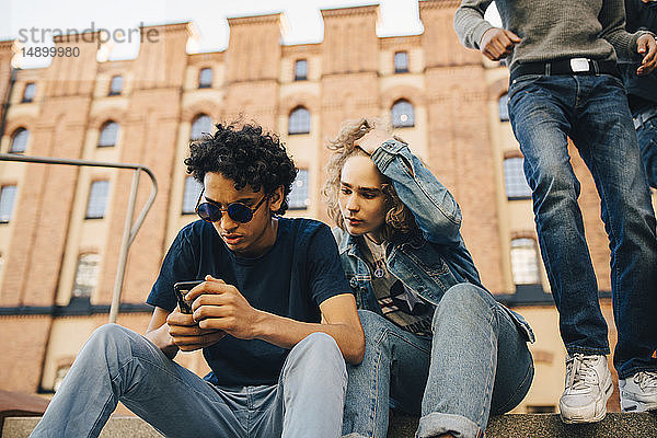 Teenager benutzt Mobiltelefon  während er in der Stadt bei einem Freund sitzt
