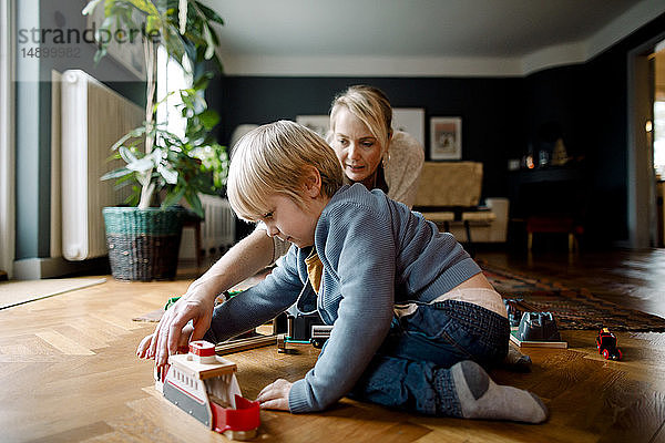 Mutter und Tochter spielen zu Hause mit der Spielzeugeisenbahn auf dem Hartholzboden im Wohnzimmer