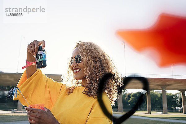 Lächelnde junge Frau fotografiert mit der Kamera gegen den Himmel bei einer Veranstaltung an einem sonnigen Tag