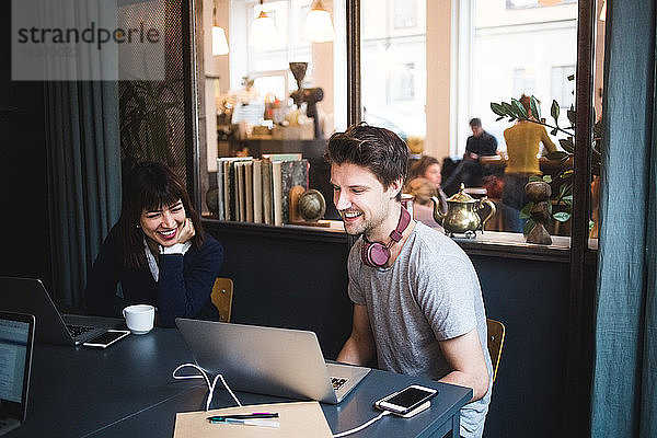 Lächelnde weibliche und männliche Kreativprofis diskutieren über Laptop am Schreibtisch im Büro