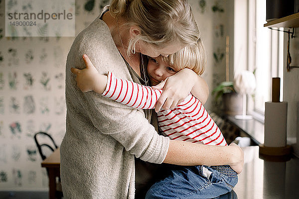 Liebende Tochter umarmt Mutter  während sie zu Hause auf dem Küchentisch sitzt
