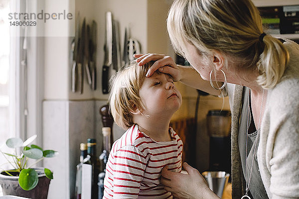 Pflegende Mutter schaut auf das geprellte Auge ihrer Tochter in der Küche