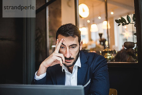 Müde Geschäftsmann schaut auf Laptop im Kreativbüro