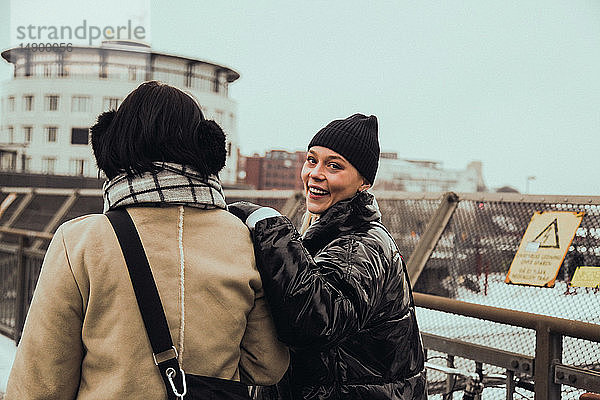 Porträt einer fröhlichen jungen Frau mit Freundin  die im Winter in der Stadt auf der Straße steht
