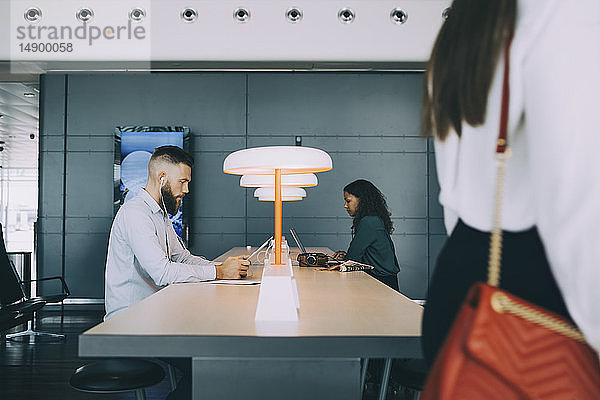 Kollegen  die Technologien nutzen  während sie am Tisch sitzen und im Abflugbereich des Flughafens warten