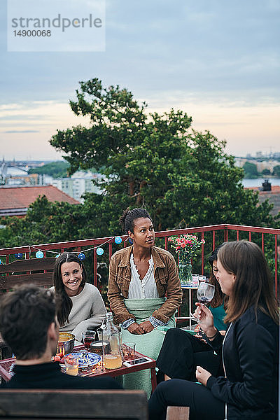 Fröhliche Freunde genießen das gesellige Beisammensein auf der Terrasse bei Sonnenuntergang