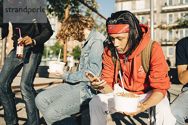 Junger Mann telefoniert mit dem Handy  während er von Freunden in der Stadt zum Essen eingeladen wird