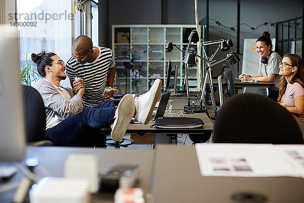 Männliche Unternehmer lächeln  während sie sich am Schreibtisch im Kreativbüro begrüßen