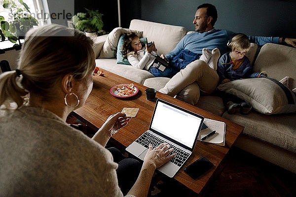 Mutter online einkaufen  während Mann und Töchter verschiedene Technologien im Wohnzimmer nutzen