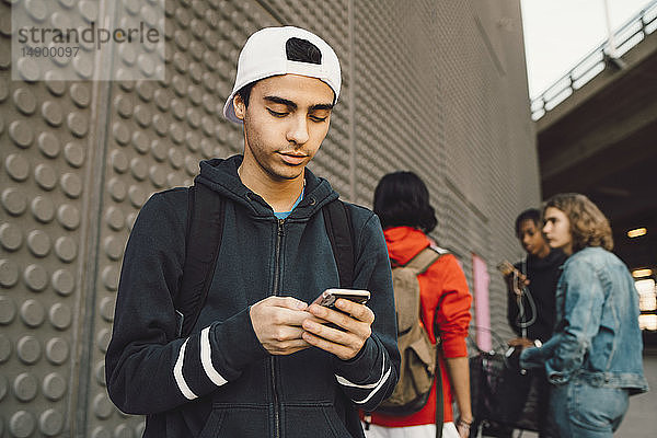 Junger Mann telefoniert mit Freunden im Hintergrund auf einem Fußweg