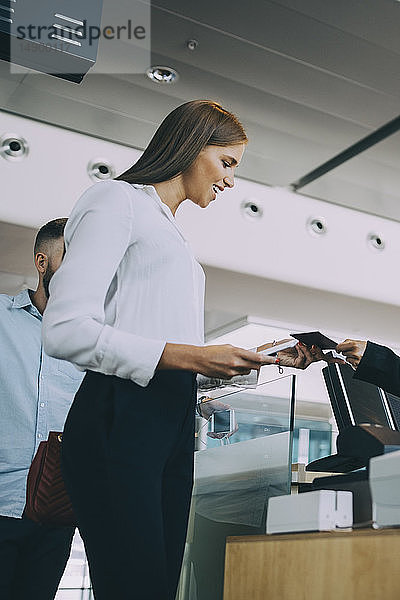Niedriger Blickwinkel auf eine lächelnde junge Geschäftsfrau beim Einchecken am Flughafen