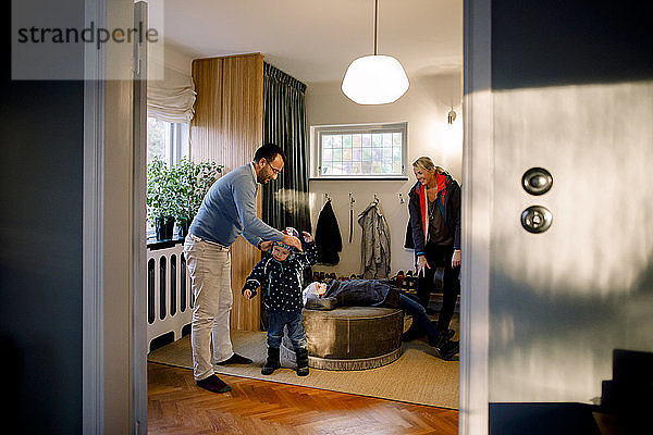 Vater hilft Tochter beim Anziehen und wird zu Hause durch die Tür gesehen