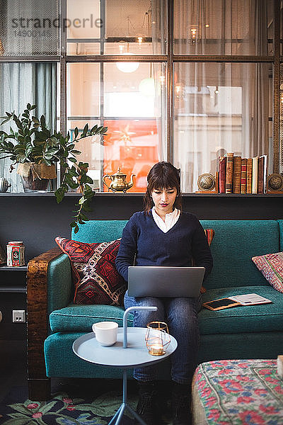 Selbstbewusste weibliche Fachkraft in voller Länge mit Laptop auf dem Bürosofa sitzend